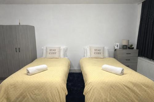 two beds in a room with yellow sheets and pillows at The Stadium Rooms Elegant and Comfy Stay in London