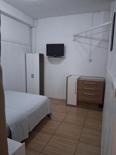 a bedroom with a bed and a tv on a wall at Kitnet Avenida in Imbituba