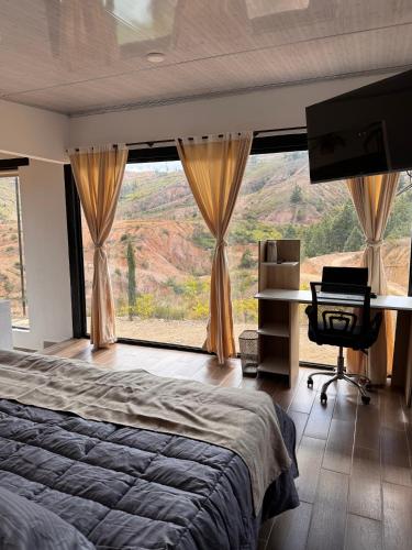 Schlafzimmer mit einem Bett, einem Schreibtisch und einem großen Fenster in der Unterkunft Glamping Eclipse Mirador Jarana Villa de Leyva 