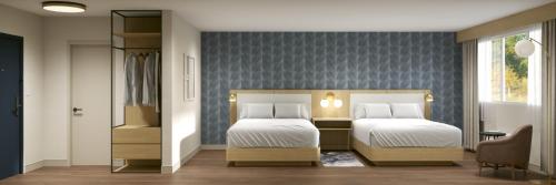 a bedroom with two beds and a blue wall at Hotel Kelowna & Conference Centre in Kelowna