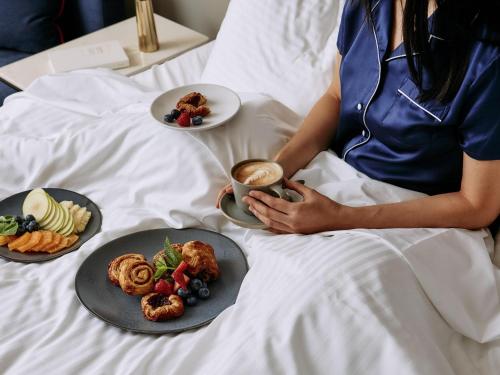 une femme assise sur un lit avec des assiettes de nourriture dans l'établissement Mercure Melbourne Doncaster, à Doncaster