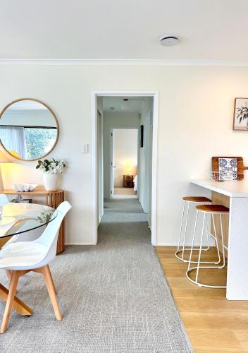 a white living room with a table and a mirror at Relaxed Mount Getaway Close to Beach & Town in Mount Maunganui