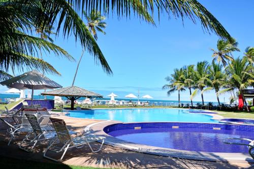 a pool with chairs and palm trees and the ocean at Residencia Bali Bahia in Praia do Forte