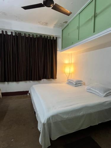 a bedroom with a large white bed with a ceiling fan at Nagaon Homestay in Nowgong
