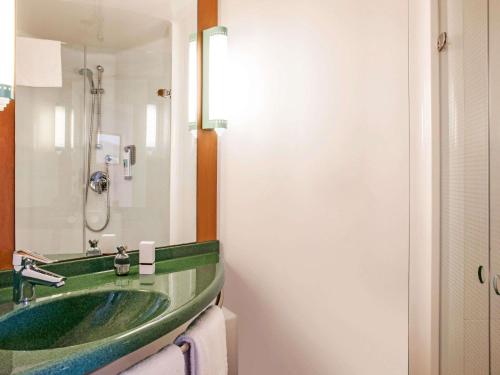ein Badezimmer mit einem grünen Waschbecken und einem Spiegel in der Unterkunft Ibis Barcelona Molins de Rei in Molins de Rei