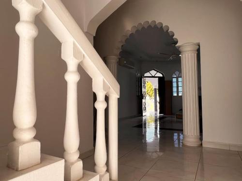 ein Flur mit weißen Säulen und einem Treppenhaus in der Unterkunft Amour Hostel in Seeb