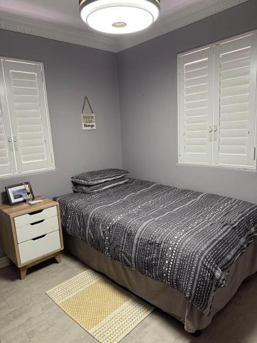 a bedroom with a bed and a nightstand and two windows at Casa Mia in Jeffreys Bay