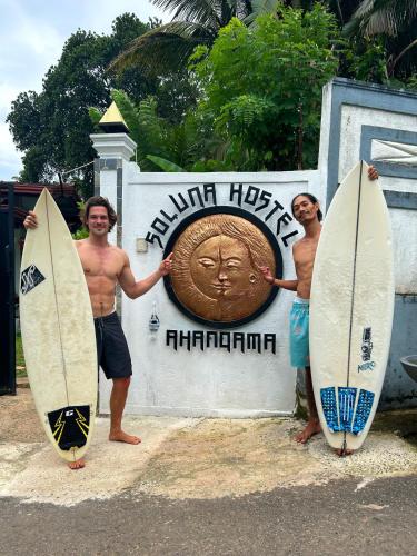 Twee mannen met hun surfplanken voor een bord. bij Soluna Hostel in Ahangama