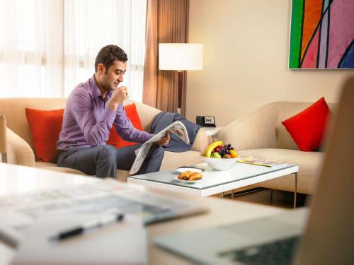 a man sitting on a couch reading a newspaper at Ibis Abu Dhabi Gate in Abu Dhabi