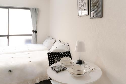 a white bedroom with a bed and a table with cups and saucers at Hani Stay Fukuoka Kaizuka-Timesカーシェアあり- in Fukuoka