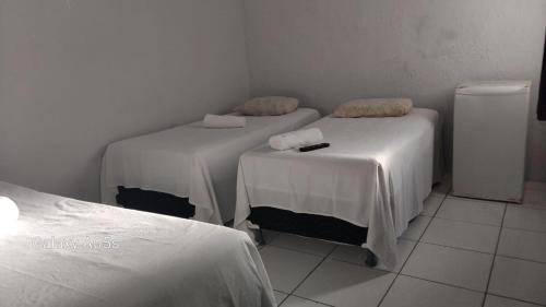 a room with two beds with white sheets and a refrigerator at Pousada praia avenida in Maceió