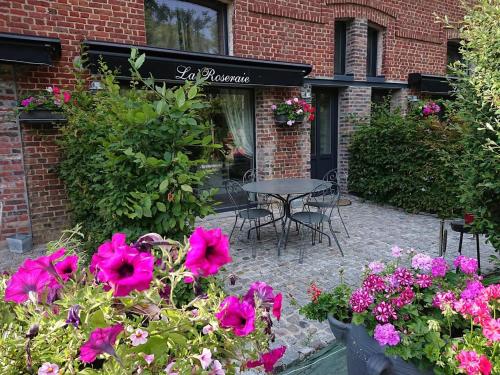 eine Terrasse mit rosa Blumen, einem Tisch und Stühlen in der Unterkunft Gîtes de la maison du haras in Beuvron-en-Auge