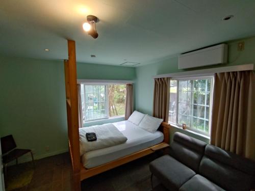 a bedroom with a bed and a couch and two windows at Nemurupa Garden Hostel and Yoga near Narita Airport 15 min Late Check in in Narita