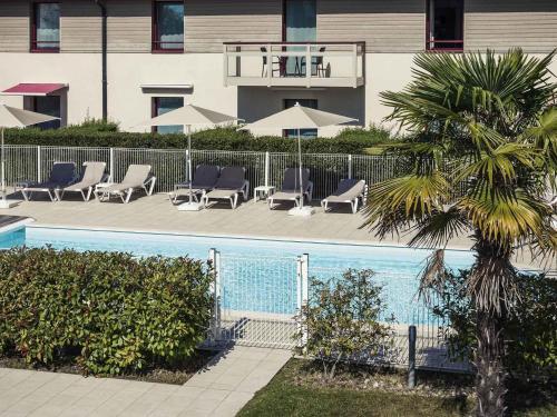 une piscine avec des chaises et un palmier à côté d'un bâtiment dans l'établissement Mercure Dinan Port Le Jerzual, à Dinan