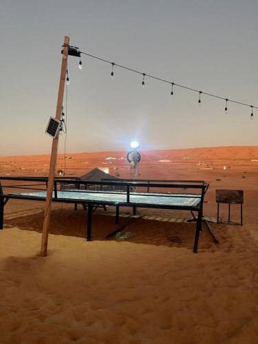 een picknicktafel in het zand met een lamp bij ESCAPE cAMp2 in Badīyah