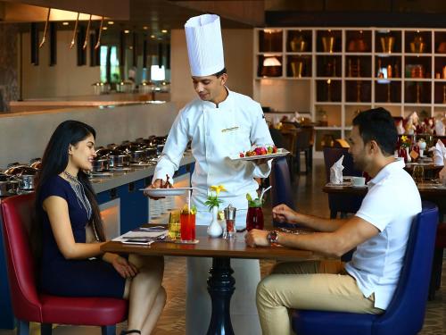 Drie mensen zitten aan een tafel in een restaurant met een chef-kok. bij Grand Mercure Mysore - An Accor Brand in Mysore