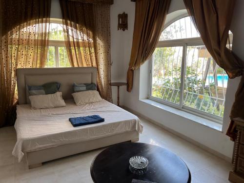 a bedroom with a bed and a table and windows at South Hammamet Pool Villa in Hammamet Sud