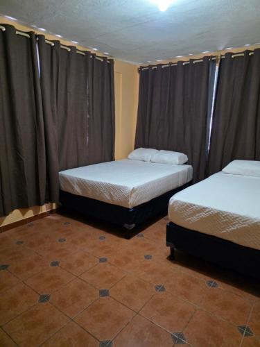 Twee bedden in een kamer met gordijnen en een tegelvloer. bij Hotel y Restaurante Punta Corona in Acajutla