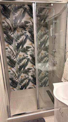 a shower stall in a bathroom with a leaf wallpaper at Central Apartments in Zaječar