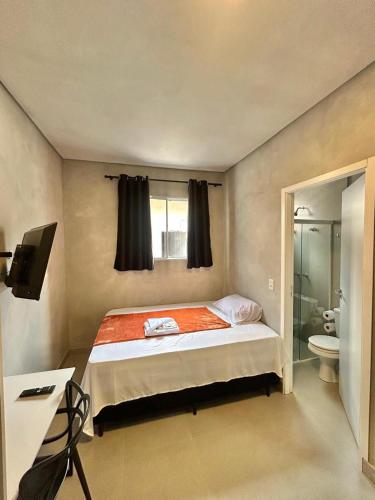 a bedroom with a bed and a toilet and a television at #108 Suíte Acolhedora com vaga Centro de Itatiba in Itatiba