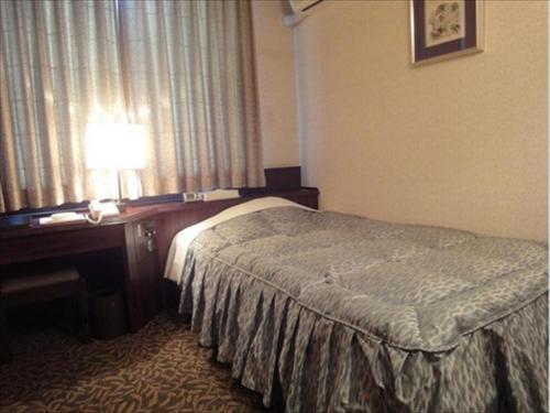 a hotel room with a bed and a desk with a lamp at Hotel CROWN HILLS MIYOSHI in Miyoshi