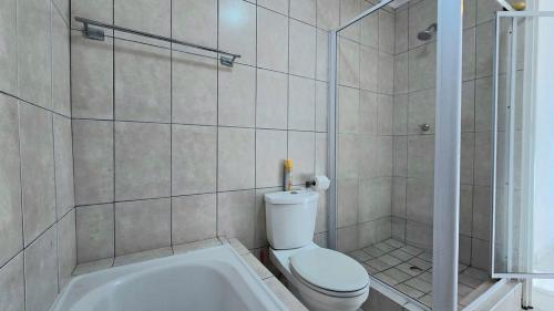 a bathroom with a shower and a toilet and a tub at Steps from the beach , Muizenberg home in Muizenberg