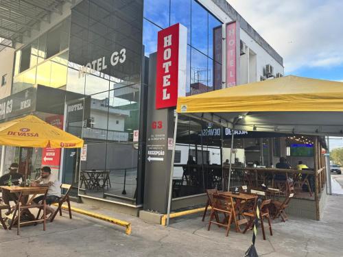 un gruppo di tavoli e sedie di fronte a un edificio di Hotel e Conveniência G3 a Teixeira de Freitas
