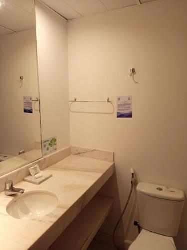a bathroom with a sink and a toilet and a mirror at Bussines Flat Iguatemi in Salvador