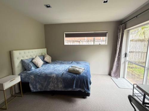 een slaapkamer met een bed met een blauw dekbed en een raam bij Sunny garden view suite with private bathroom in Auckland