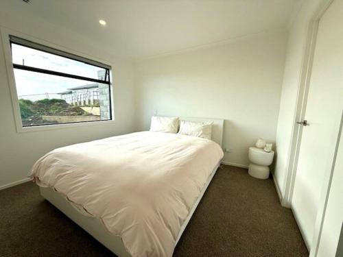 ein weißes Schlafzimmer mit einem großen Bett und einem Fenster in der Unterkunft Light-Filled Coastal Hideaway in Raglan