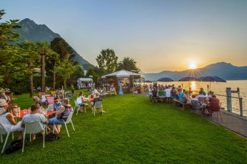 a group of people sitting in chairs on the grass by the water at Seerausch Swiss Quality Hotel in Beckenried