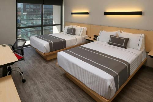 a hotel room with two beds and a desk at City Express Plus by Marriott Monterrey Galerías in Monterrey