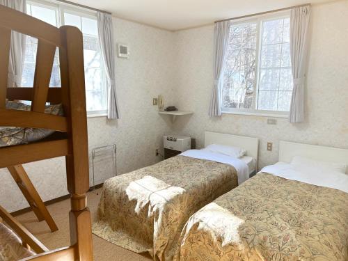 a bedroom with two beds and two windows at ペンション風と旅のアトリエ in Tateshina