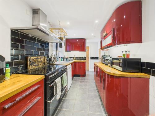 een grote keuken met rode kasten en apparaten bij Cosy Cornish Cottage with Firepit & Parking in Newlyn East