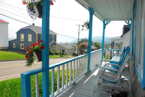 a blue rocking chair on a porch with a view of a street at Maison de campagne le Nichouette in Les Éboulements