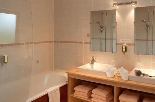 uma casa de banho com uma banheira, um lavatório, uma banheira e um espelho. em Hotel Neuhauser em La Broque