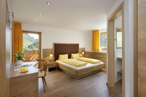 a bedroom with a bed and a desk and a table at Garni-Hotel Wiesental in Pfelders