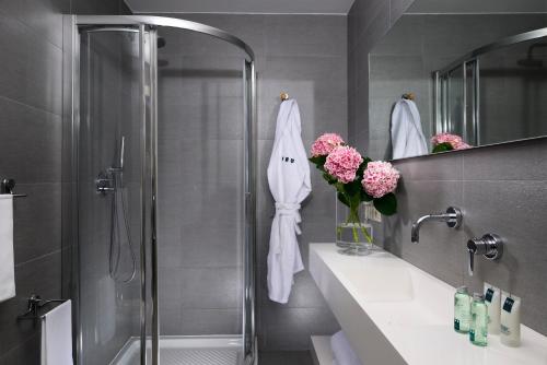 a bathroom with a shower and a vase of pink flowers at UNAHOTELS Forte Dei Marmi in Forte dei Marmi