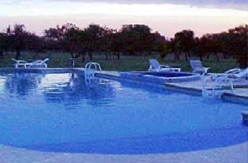 una gran piscina con agua azul y sillas blancas en El Espinillo en Merlo