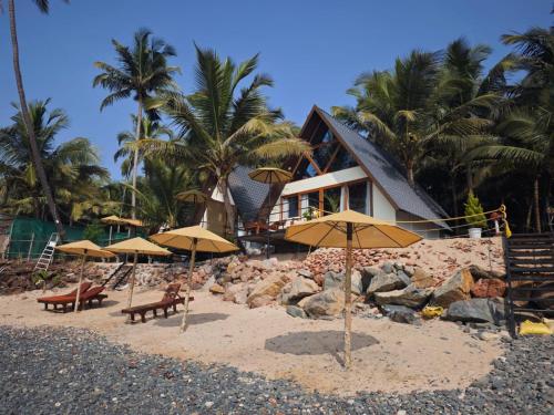 a beach with umbrellas and chairs and a house at Colomb Beach Cottages in Patnem