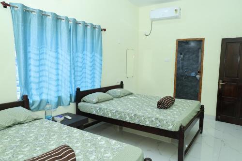 two beds in a room with blue curtains at VAISHVI Homestay in Kāsarkod