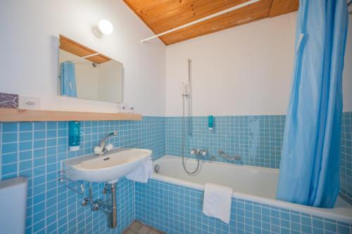 een blauw betegelde badkamer met een wastafel en een bad bij Hotel Haus am Waldrand in Flims