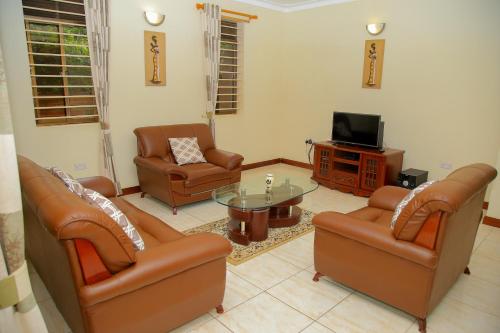 een woonkamer met lederen meubels en een televisie bij CALM SUITES KAMPALA in Kampala