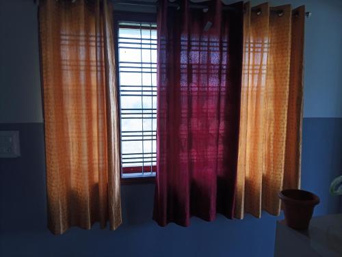 a window with orange and red curtains in a room at Rooms & Food Sri Ranga in Belūr
