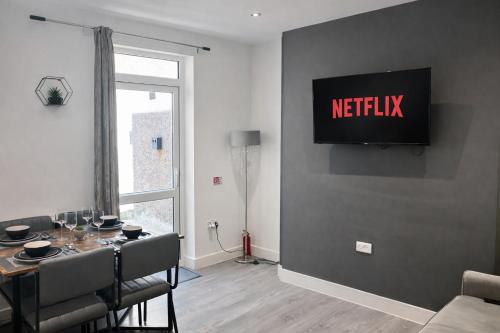 a living room with a table and a television on a wall at Emerald Living, 4 bedrooms, sleeps 6, free parking, close to centre and beaches! in Swansea