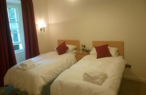 a room with two beds with white sheets and red pillows at Byrdir House in Harlech