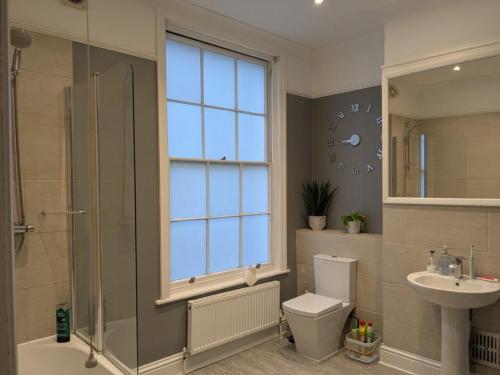 ein Badezimmer mit Waschbecken, Toilette und einer Uhr an der Wand in der Unterkunft Seaside 3 bed terraced house in Hastings