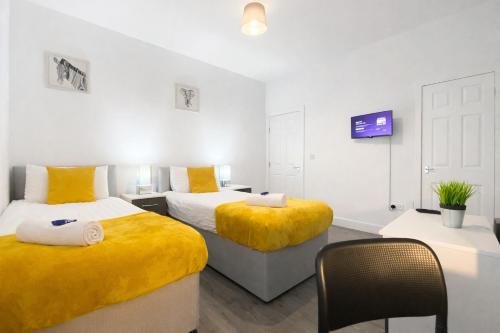 a bedroom with two beds with yellow sheets and a tv at Emerald Living - Hanley, Stoke-on-Trent, sleeps 5, with free parking! in Stoke on Trent