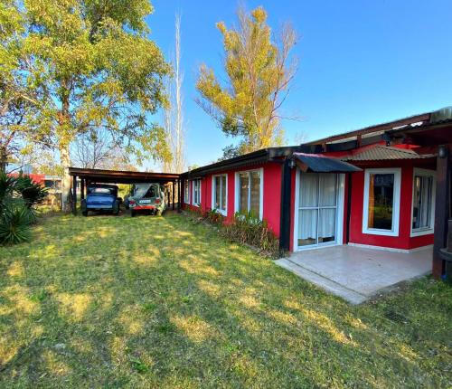 een rood huis met een garage naast een tuin bij La Arboleda - Casa de Campo in Marcos Paz