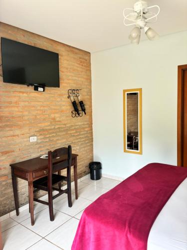 a bedroom with a desk and a tv on a wall at Villa Cottage Pousada in Monte Alegre do Sul